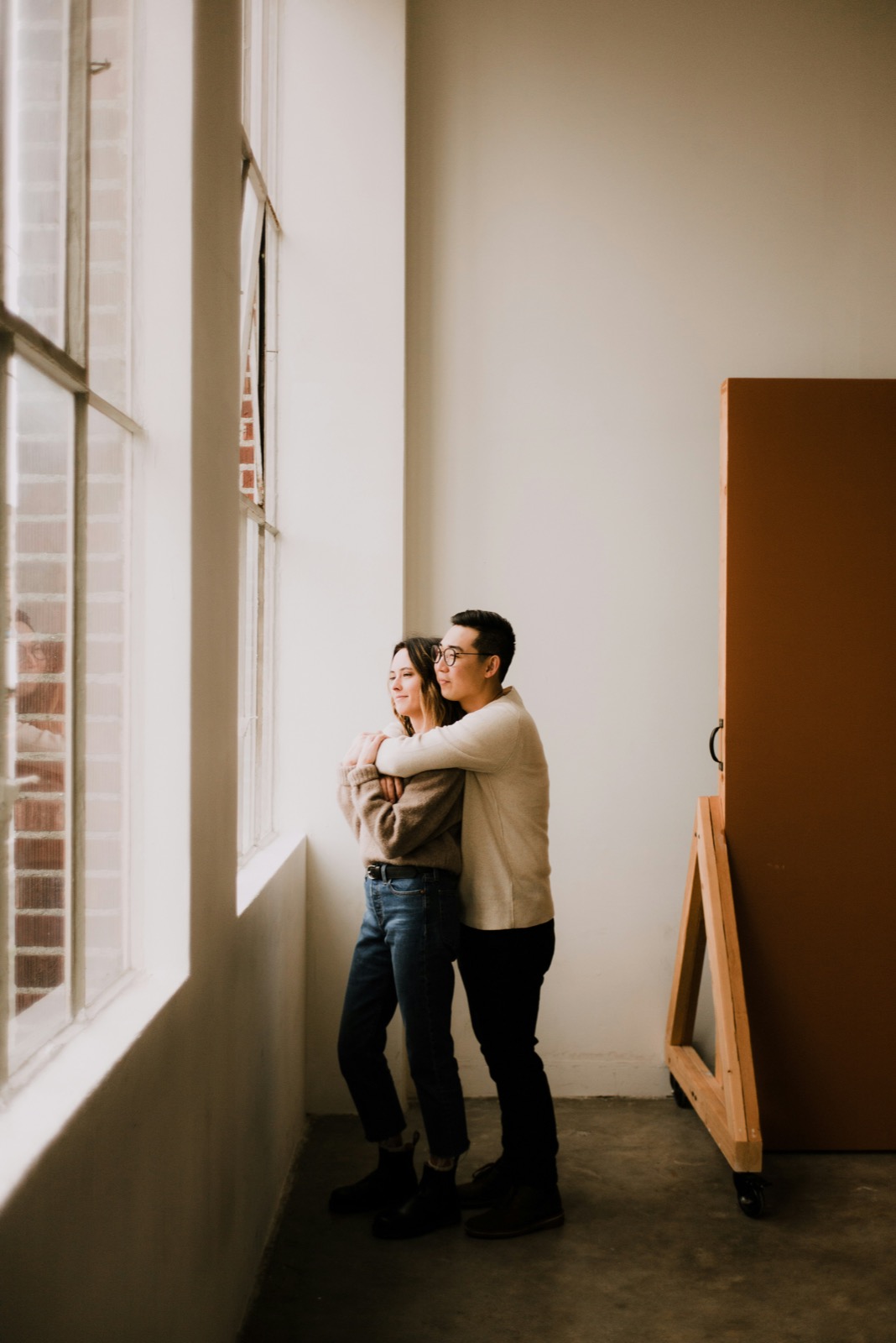 Pareja joven en abrazo contemplativo mirando hacia la luz natural · planificación familiar